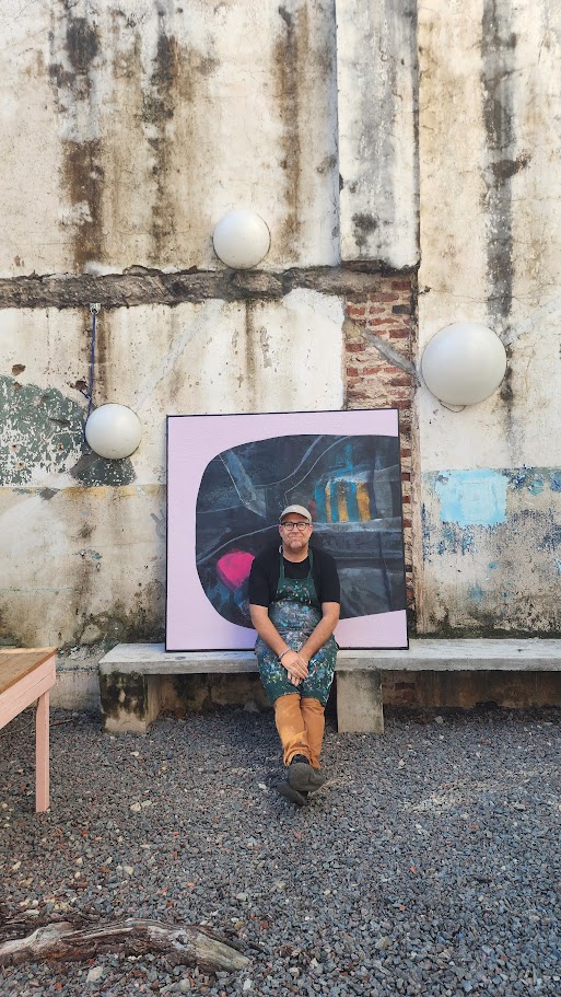 Artista en el patio de Chancho Libre Arte, Castelli 150. La obra apoyada en la pared de cemento, el delantal, la luz de tarde.