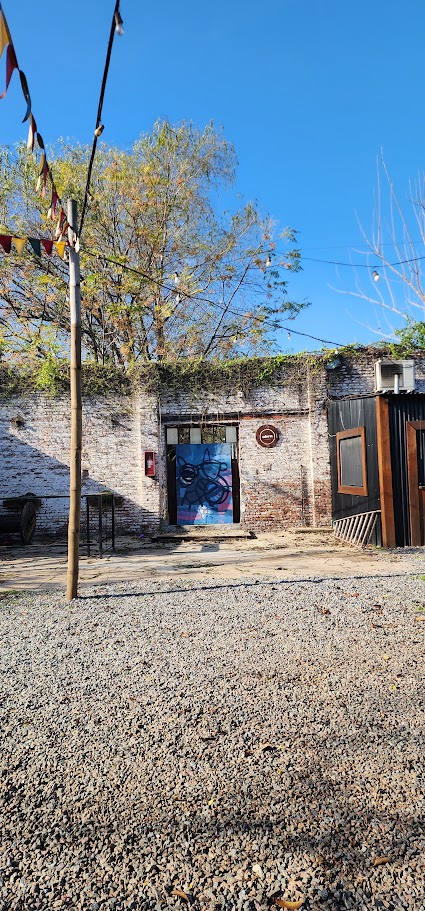 Chancho Libre Arte, Castelli 150, Tigre. El patio de grava y ladrillo visto de día. Una fachada que mezcla galpón industrial con intervención artística.